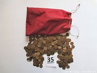 Bag of worn copper U.S. wheat pennies spilling out of red drawstring pouch, showing quantity and storage method.