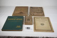 Group shot of five geography and world atlas books including one green hardcover, one german atlas, two tan bound atlases and one paperbound geography