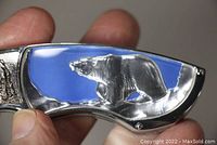 Close-up of folding pocketknife handle featuring embossed silver-tone Alaskan polar bear on blue background.