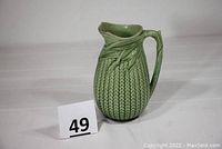 Front angled view showing full pitcher with ear of corn textured body, green glaze, and broken spout.