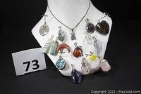 Display of 15 assorted gemstone and glass pendants on white mannequin bust against black background, showing variety of colors and shapes.