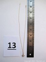 Full view of gold chain necklace alongside ruler showing 17" length and pendant.