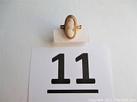 Top-down view of the vintage 10 KT gold cameo ring showing the full profile of the lady carved in the cream and brown cameo stone, placed on a white stand next to a lot number card.
