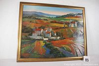 Full view of lacquered print showing European countryside with buildings, fields, and hills in warm tones with bright red roofs and clear lacquer coating visible.