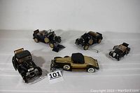 Five model cars arranged on a white surface; includes two 1939 Ford Model A convertibles, one 1932 Ford coupe, one 1934 Ford coupe, and one 1931 Rolls Royce model radio missing a front wheel, showing scale and condition.