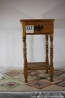 Front view of the maple end table with single drawer, turned legs, and lower shelf, placed on colorful geometric accent rug.