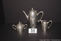Three-piece stainless steel coffee set arranged on black background with lot number 55 visible