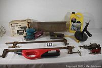 Photo showing all tools in the lot including Black & Decker jigsaw, Makita hand sander, Arrow electric staple tool, heavy duty table vice, drain auger, 24-inch bar clamps, air pump, wooden miter box and Prestone antifreeze gallon.