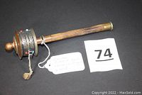Full view of the prayer wheel showing wooden handle, brass/copper wheel embossed with mantras and stones, leather strip with attached weight.