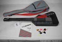 Full view of the UNISYNTH electronic guitar model XG-1 laid out with gray carrying case, instruction manual, and assorted guitar picks.