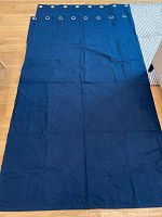 View of one full navy blue curtain panel laid flat on floor, showing full length and width with wrinkling visible.
