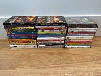 Three stacks of assorted DVD and Blu-ray disc cases laid out on floor.