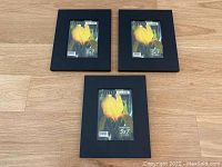 Three matte black 5x7 photo frames, arranged on a wooden floor, showing front view with product labels visible