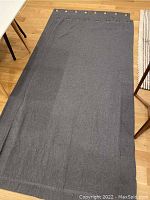 Full view of one grey curtain panel laid out flat on wooden floor, showing the fabric and overall size.