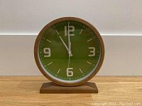 Front view of the decorative green clock showing face, numerals, and hands.