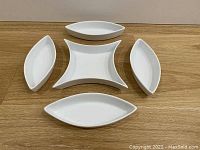 Photo of five individual white ceramic serving dishes arranged separately on wooden surface.