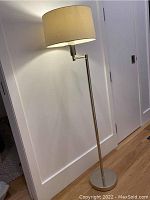 Full view of metal floor lamp with articulated arm and fabric shade, showing height and lamp structure.