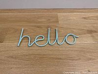 Full top-down view of the blue metal 'hello' sign on a wooden surface, showing entire word and shape.