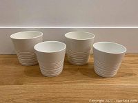 Front view of all four white IKEA Muskot plant pots arranged in a line on a wooden surface