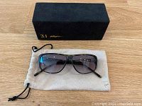 Photo showing sunglasses on beige dust bag and black carrying case with gold 3.1 Phillip Lim logo.