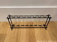 Clear shot of the test tube bud vase showing 7 glass tubes horizontally placed in a black metal frame on a wooden surface against a plain background.