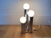 Front view of vintage chrome tri-light lamp with all bulbs illuminated on wooden floor.