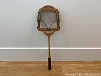 Full view of the vintage Dunlop wooden badminton racquet with leather wrapped grip and attached stretcher.