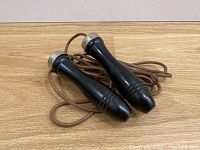 Entire jump rope coiled with visible wooden handles and leather-like rope laid out on wood surface.