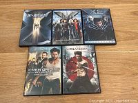 Photo showing five DVD cases of X-Men related movies arranged on a wooden surface: X-Men, X-Men: The Last Stand, X2: X-Men United, X-Men Origins: Wolverine, and The Wolverine.