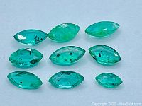 Photo of nine marquise cut Colombian emeralds arranged on flat surface, showing mixed sizes and green coloration with visible inclusions.