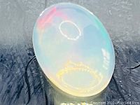 Close-up image of the oval Ethiopian opal cabochon showing rainbow flashes and glossy polished surface reflecting ambient light.