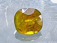 Close-up image of a cushion cut yellow sphene gemstone showing facets and reflective luster.