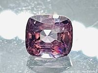 Front view of cushion-cut spinel on black reflective surface showing color and cut