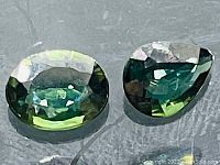 Close-up image of two oval and pear cut blue-green sapphires showing their color and clarity.