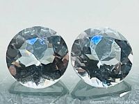 Close-up of two round diamond cut aquamarine gemstones showing facets and high clarity.