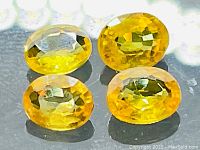 Four oval cut yellow sapphires arranged in close-up on a reflective surface.