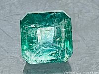 Top-down close-up photo of an emerald cut natural emerald gemstone with vibrant green color and internal inclusions.