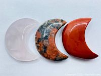 Photo of three hand carved crescent moon carvings from mixed gemstones showing front view and color patterns.