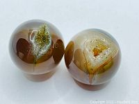 Two polished druzy agate spheres with druzy crystal formations inside, showing smooth, glossy surfaces and natural banding in neutral browns and beiges