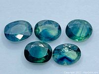 Top view showing five oval cut sapphires with tri-coloured patterns in shades of blue, green, and yellow.