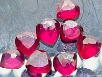Eight pear cut natural blood red rubies arranged on a reflective surface showing their facets and color vividly.