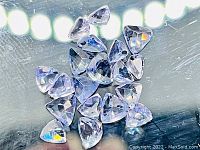 Loose natural tanzanite trillion cut gemstones displayed on reflective surface, showing light to medium blue purple color and triangular faceted shape