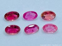 Six oval cut pink tourmaline gemstones shown together laid out on a white background, displaying color and clarity variations.