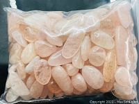 Bag of larger rough cut pink Morganite crystals, translucent with various hues and inclusions shown on a dark surface