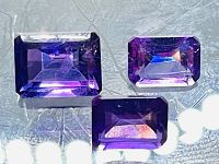 Photo showing three emerald cut deep purple amethysts with strong reflection and clarity under light.