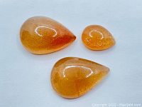 Three pear cabochon cut sunstones displayed on a white background, showing their size and color variations.