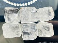 Six polished natural crystal quartz cubes displayed on black background showing transparency and surface features.