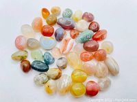 Photo showing a collection of 43 rough cut polished agate stones in varied colors including white, orange, red, blue, green, and yellow, with banding and natural patterning visible.