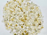 Top view showing many small clear quartz crystals with golden rutilated needle inclusions clustered together on a light surface.