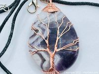 Close-up photo of natural banded amethyst pendant with copper wire tree design and hemp rope chain.